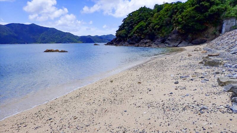 屋鈍海岸の白い砂浜と透明な海。丸みを帯びた石が点在する波打ち際の景観
